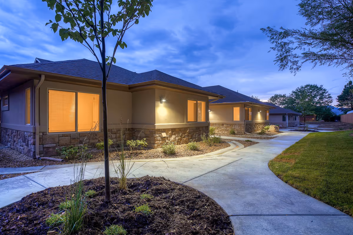 A single-story senior living facility exterior at dusk with lit windows and curved walkway.