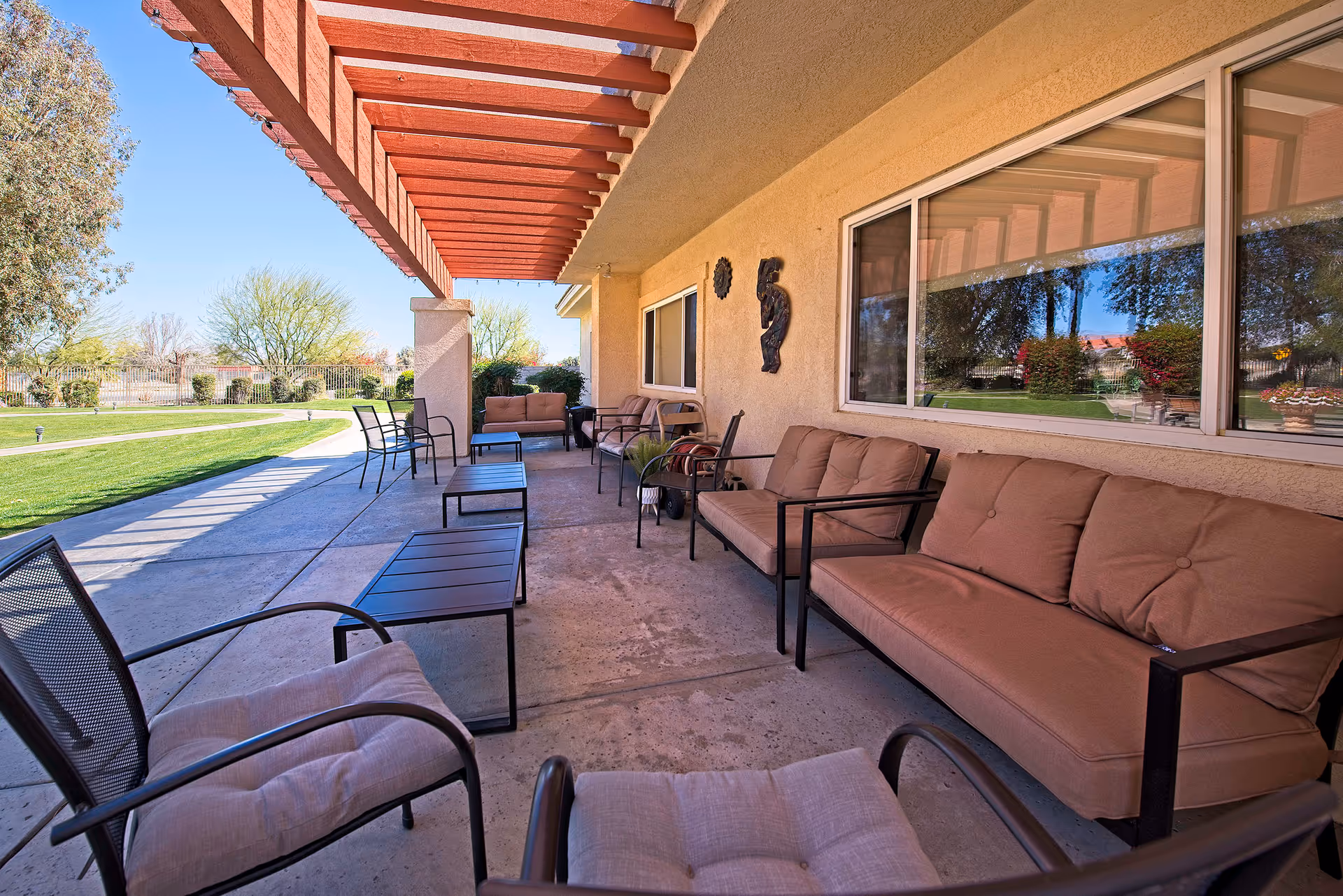 Covered outdoor patio with cushioned seating and small tables overlooking a landscaped lawn.
