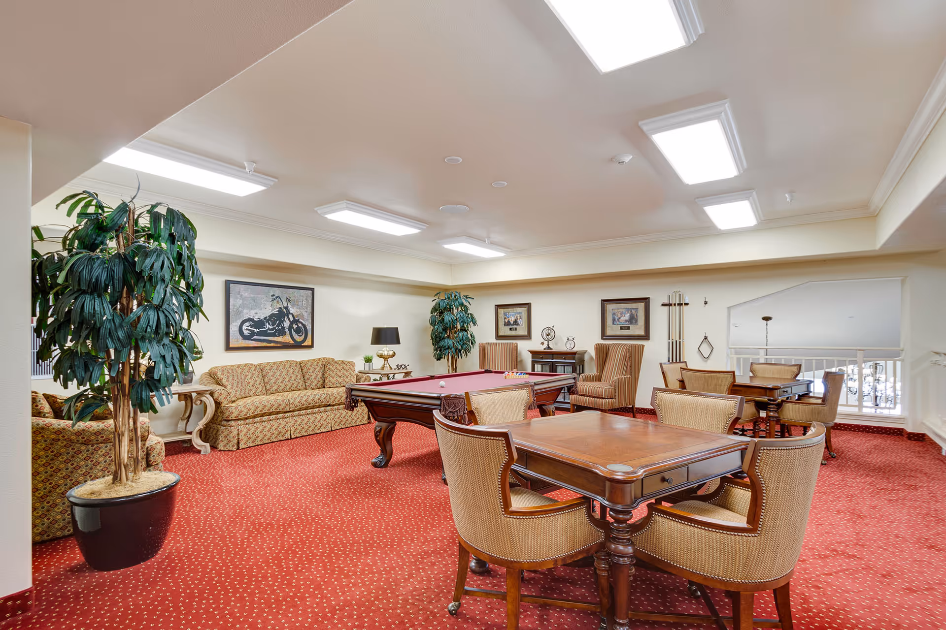 Common lounge with a pool table, card tables, upholstered sofas and chairs, and potted plants.