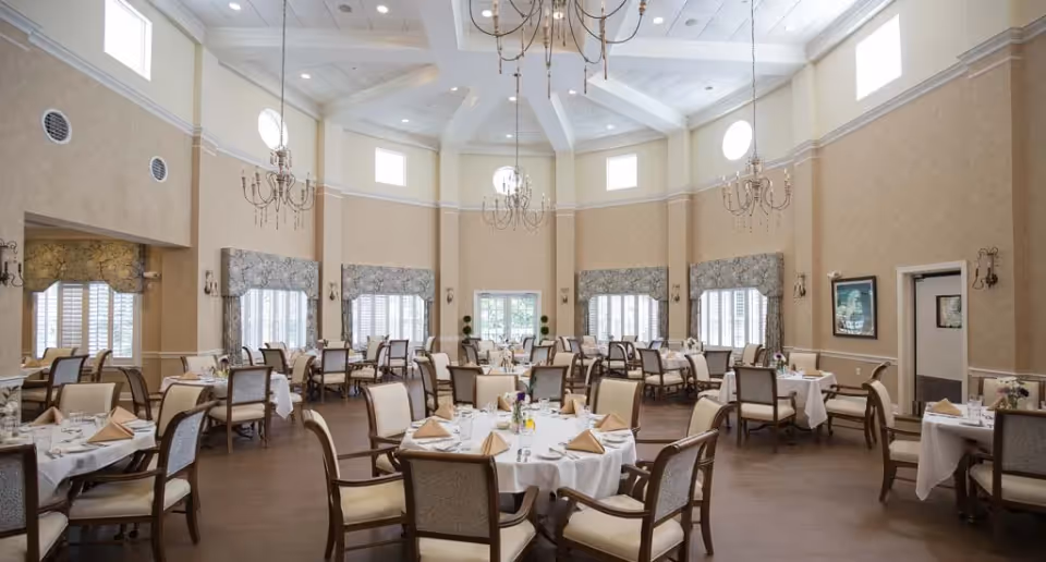 Large elegant dining room with round tables set for meals, high vaulted ceiling and chandeliers.