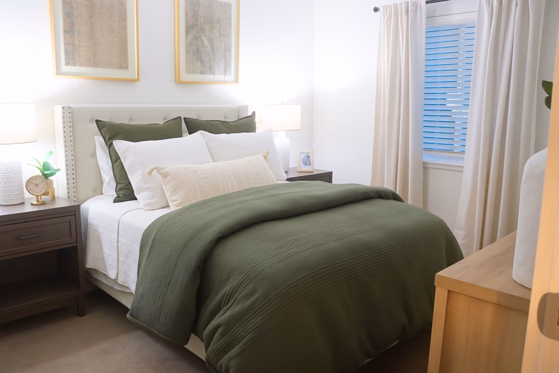 A neatly made bedroom with a bed dressed in green bedding, bedside tables with lamps, and a window with curtains.