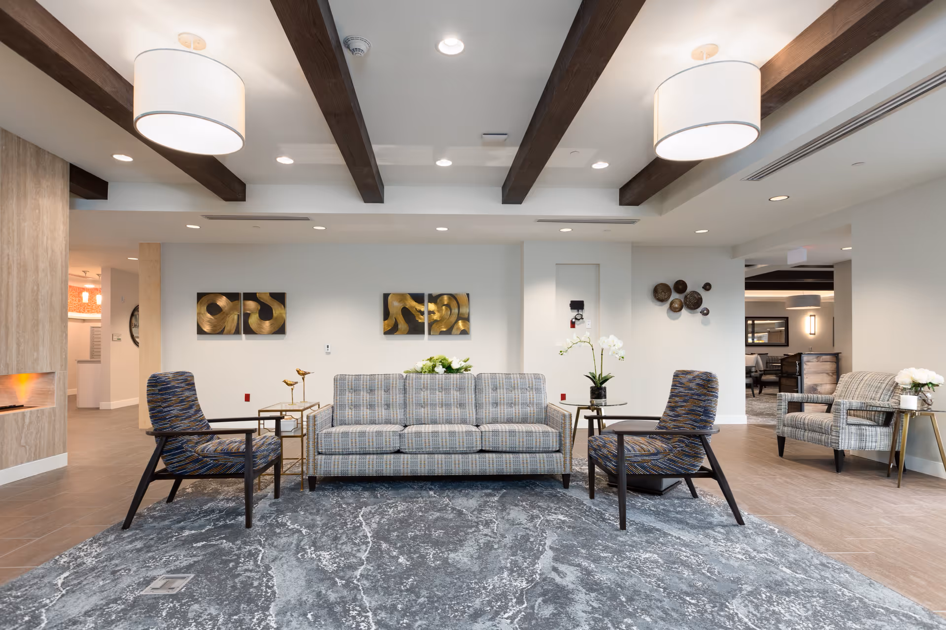 Bright modern lounge area with a sofa, armchairs, side tables, decorative wall art and exposed ceiling beams.