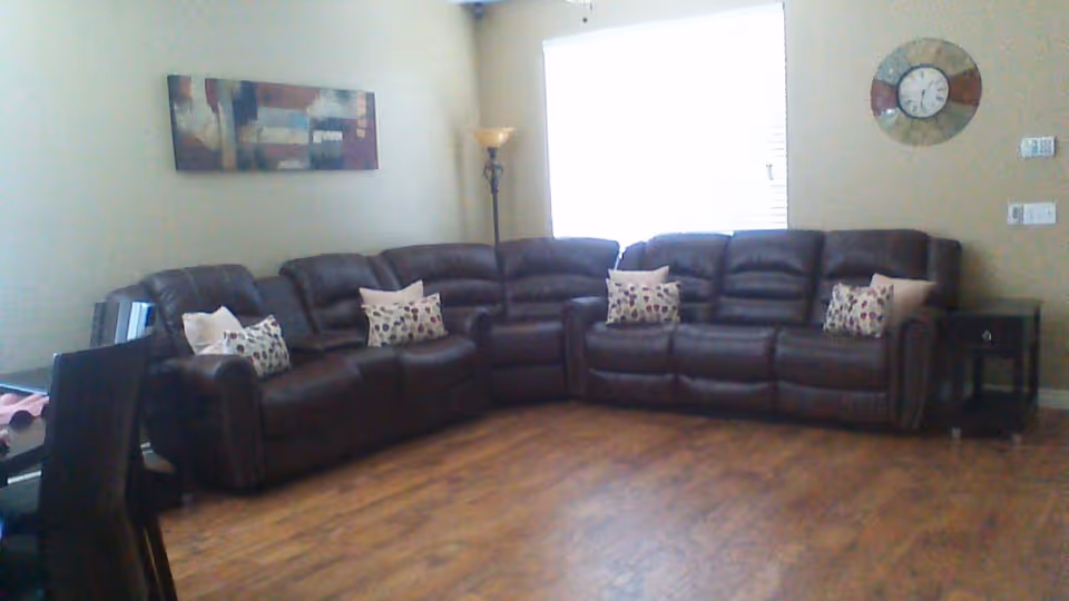 Living room with a large brown leather sectional sofa, patterned throw pillows, wall art, and hardwood floor.