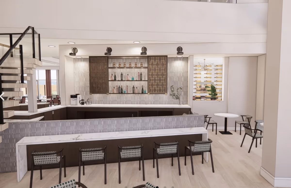 Modern communal bar and seating area with marble countertops, bar stools, tables, and a bottle display in a bright interior.