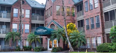 Brick senior living building with entrance, windows, balconies, and palm trees.