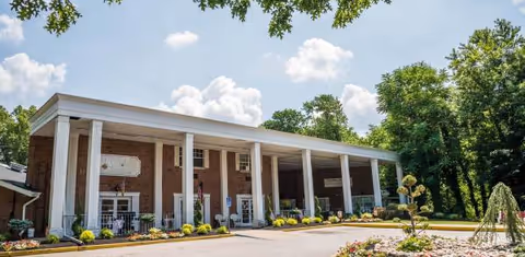 Brick building with a long white-columned entrance and manicured landscaping.