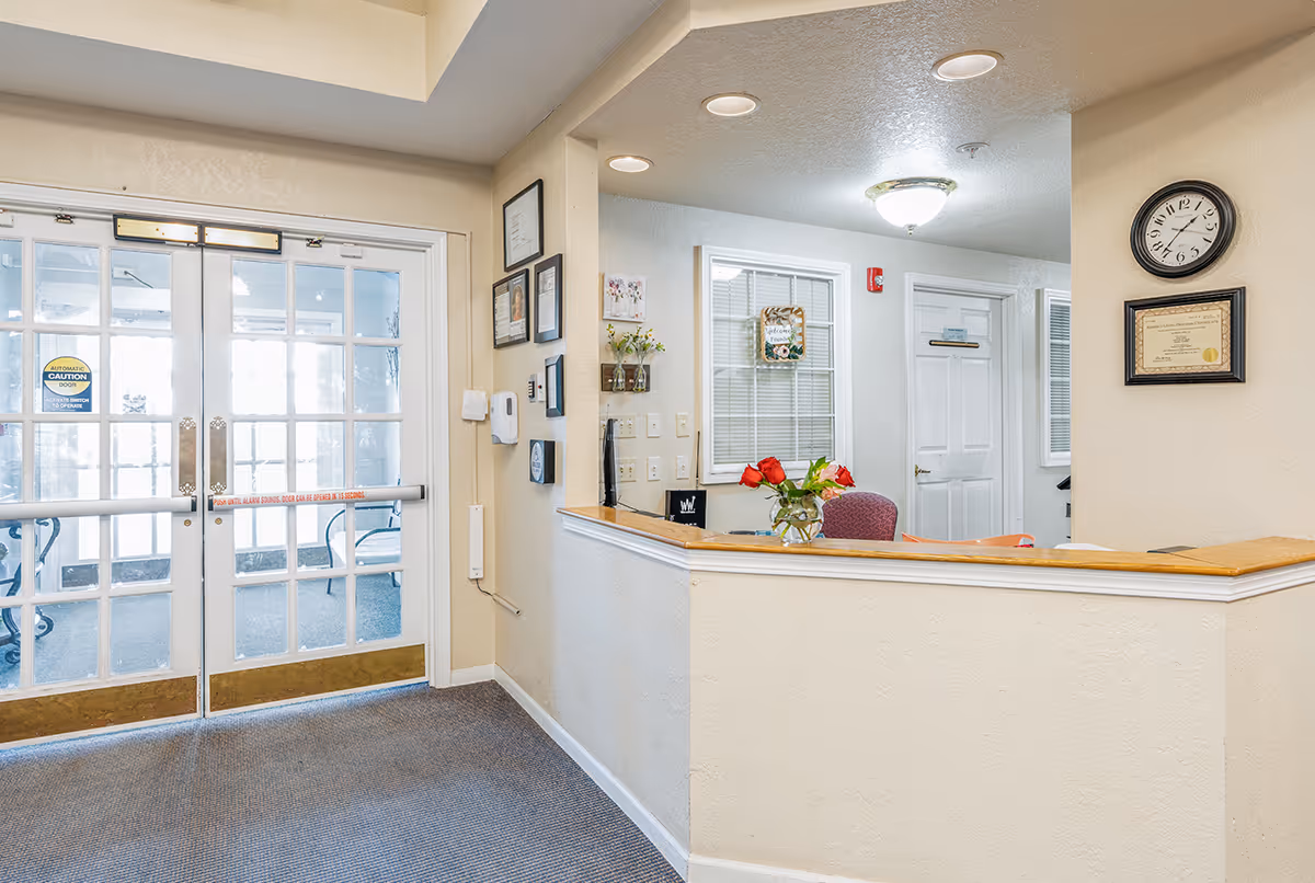 Reception area with a front desk, a vase of flowers, wall clock and double glass entrance doors.