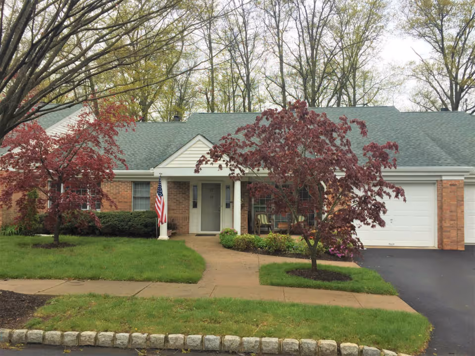 Single-story brick residence with a front porch, American flag, two red-leaf trees, garage and driveway.