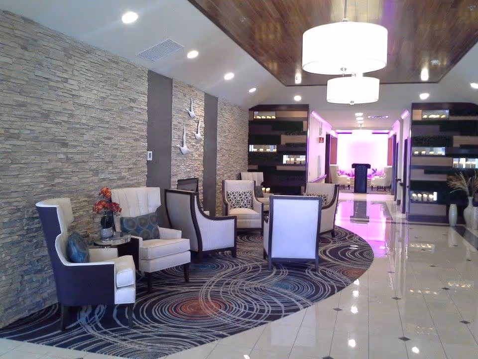 Stylish lounge with upholstered armchairs arranged on a patterned rug, a stone accent wall, pendant lights, and a softly lit corridor in the background.