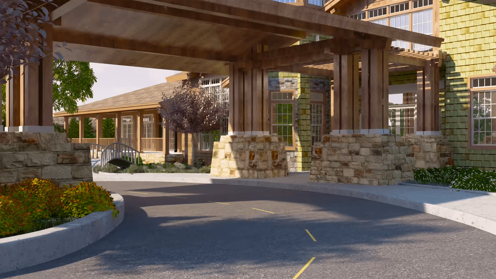 Covered driveway entrance to a building with wooden beams and stone pillars, surrounded by landscaped greenery and trees, with a pathway and a small bridge visible in the background.
