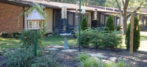 Single-story brick building with manicured front yard, shrubs, and decorative bird feeders.