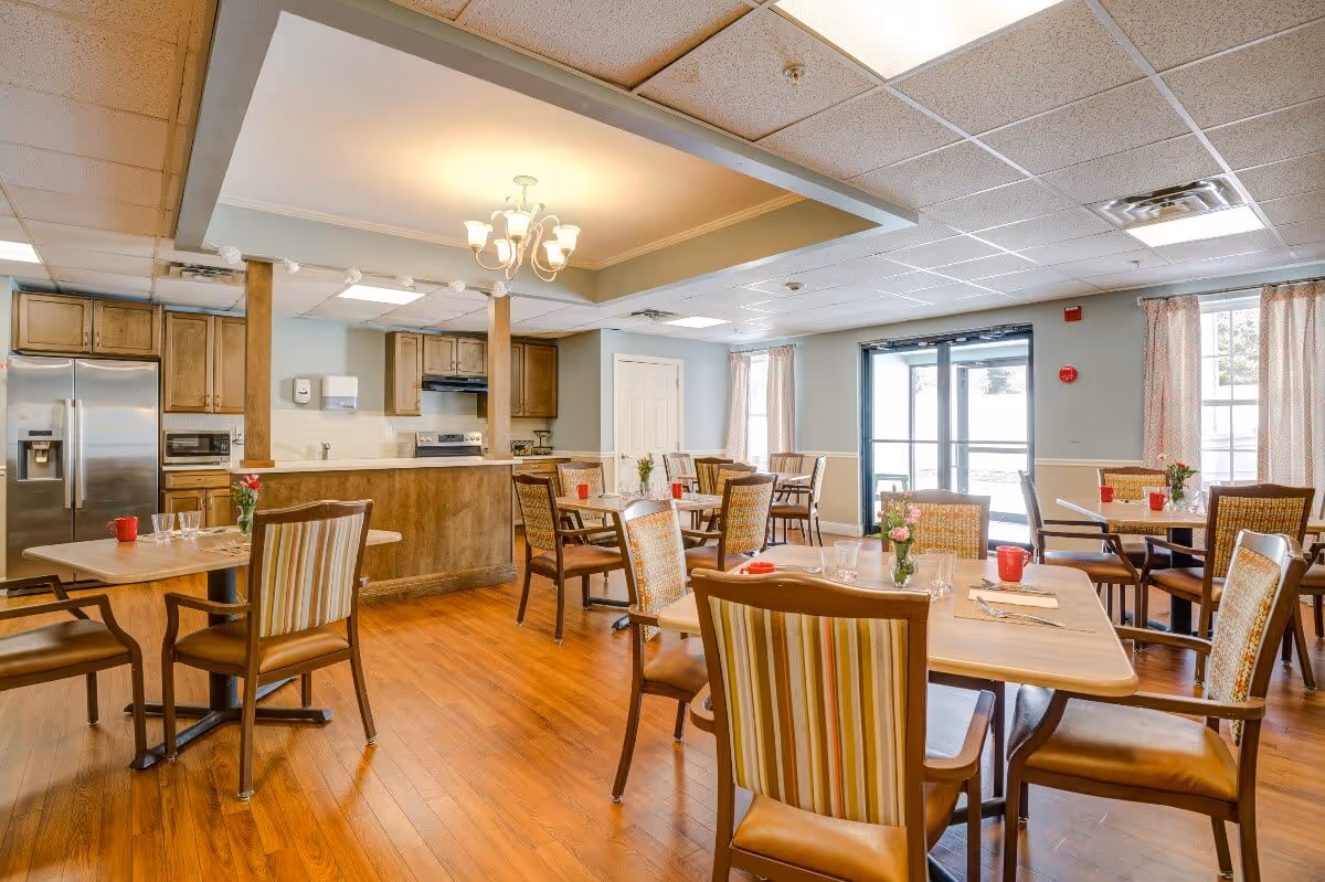 Community dining area with wooden tables and chairs, place settings, and an open kitchen in the background.
