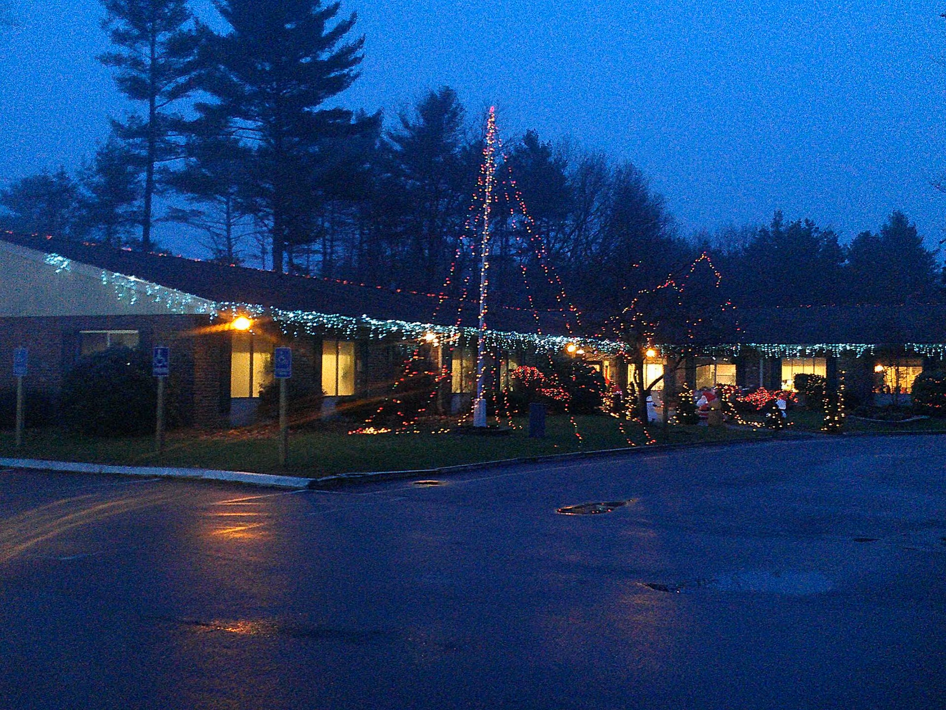 Front exterior of Sudbury Pines Extended Care at dusk, decorated with string lights and illuminated windows.