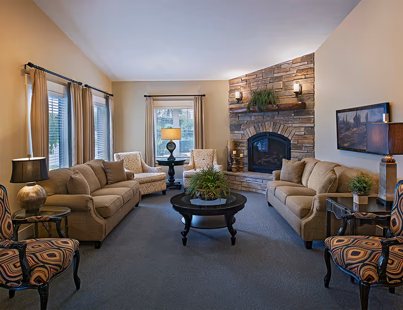 Cozy living room with sofas and armchairs arranged around a central coffee table and a stone fireplace.