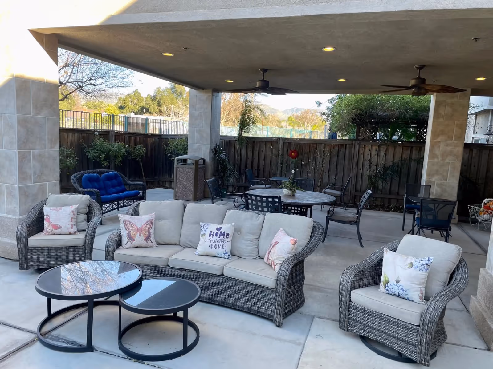 Covered outdoor patio with wicker sofas, armchairs, coffee tables and a dining table under a roof with ceiling fans.