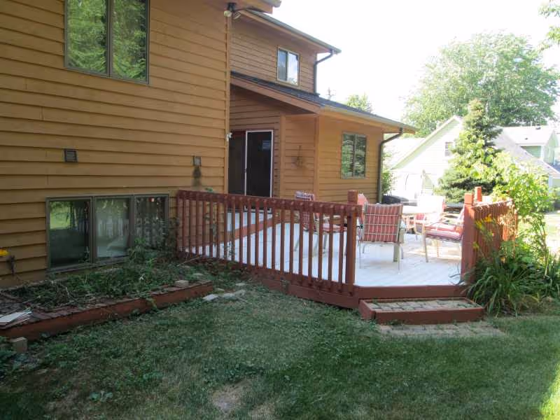 Brown two-story house with wooden deck and outdoor seating area.