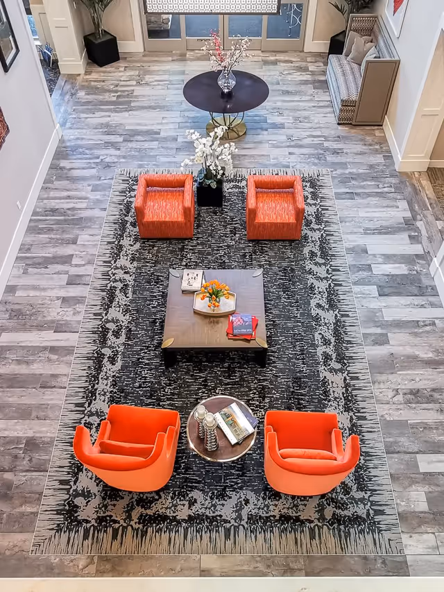 Overhead view of a senior living lobby with orange chairs arranged around a coffee table on a patterned rug.