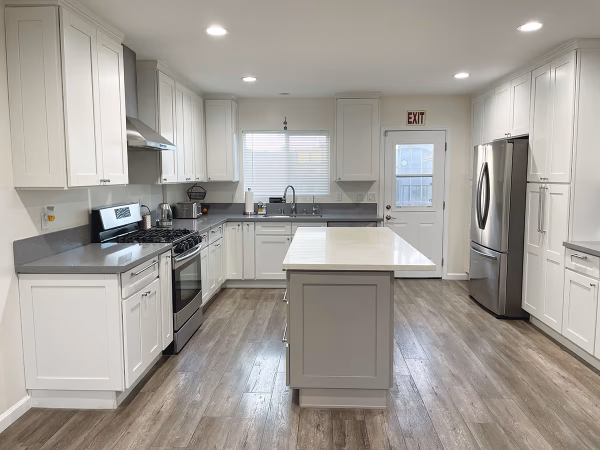 Bright modern kitchen with white cabinets, a central island, stainless steel appliances, and wood-look flooring.