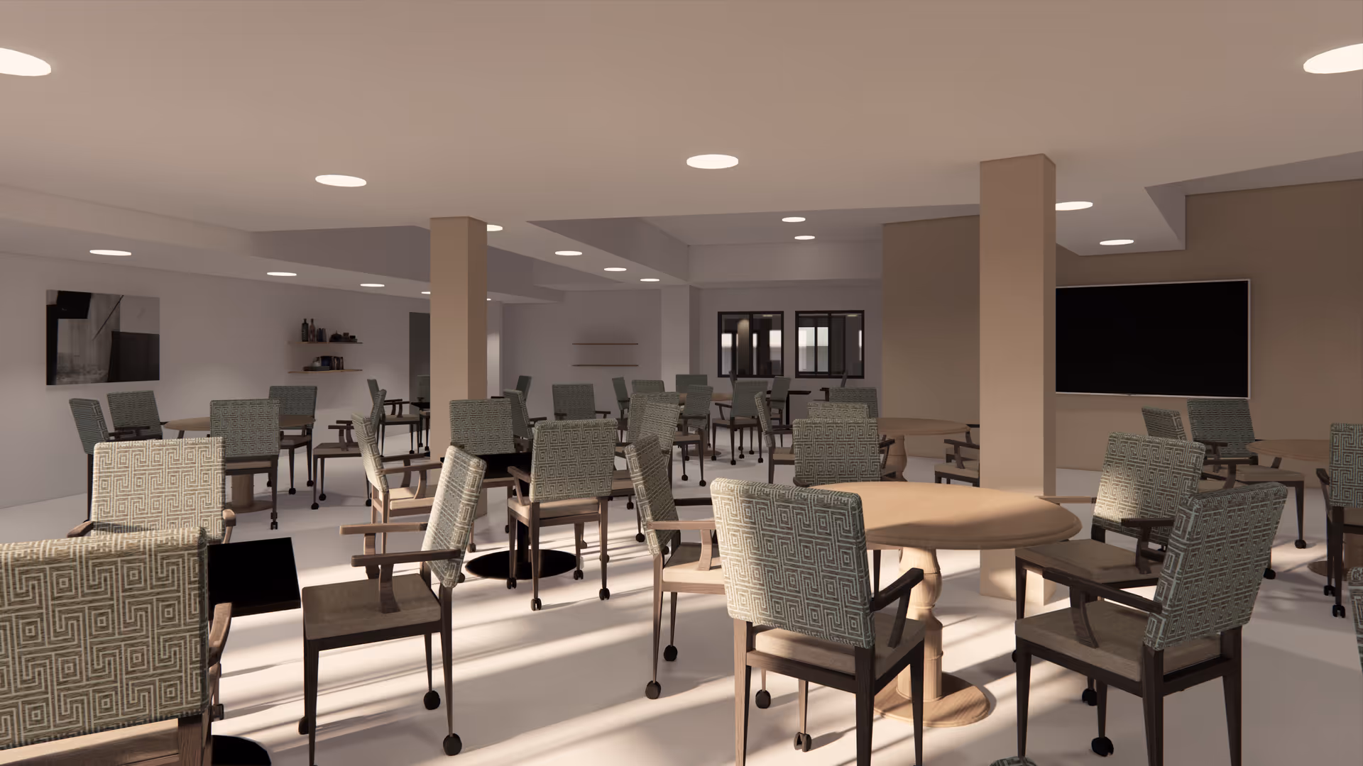 A spacious dining room with multiple round and rectangular tables surrounded by cushioned chairs on wheels. The room has a neutral color palette with beige walls and ceiling lights. There are shelves with decorative items and a large flat-screen TV mounted on the wall.