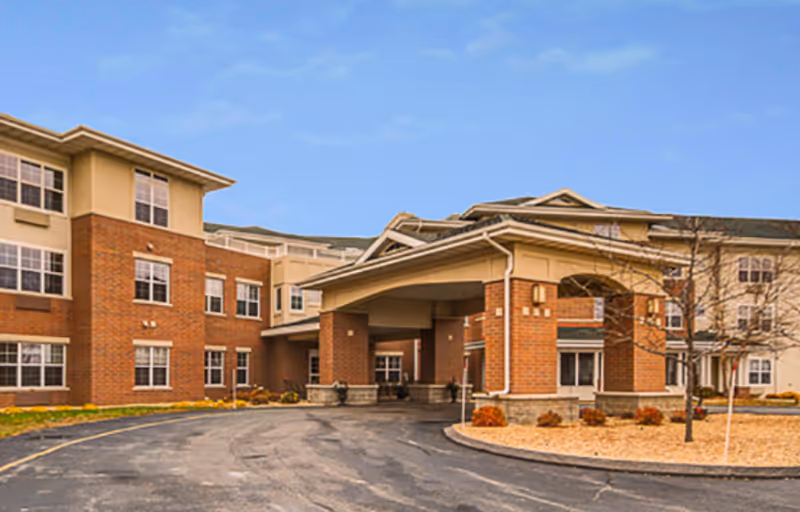 Front entrance and porte-cochere of a multi-story brick senior living facility with a circular driveway.