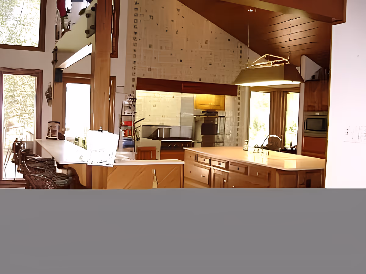 Open-plan kitchen with a large island, wooden cabinetry, pendant light, and a breakfast bar with stools.