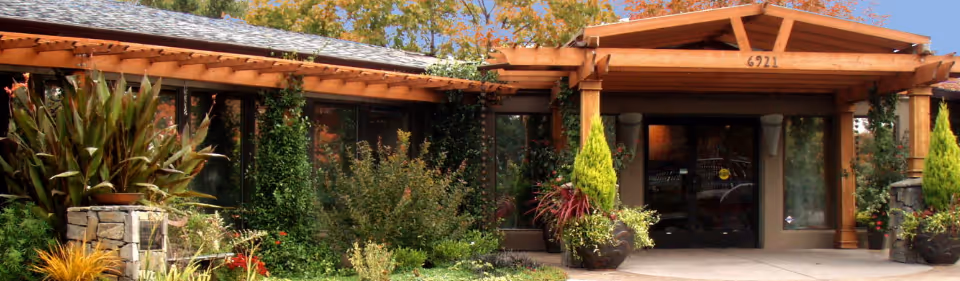 Wooden entrance canopy with glass doors and surrounding landscaping at the building front.