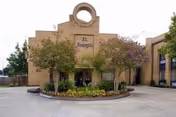 Front exterior view of St. Joseph Nursing Home building with a circular driveway, landscaped garden with trees and shrubs, and a distinctive round architectural feature at the top center of the building.