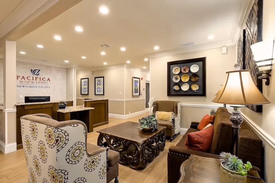 Well-lit senior living lounge with sofas, patterned armchairs, a carved coffee table, reception desk and decorative wall art.