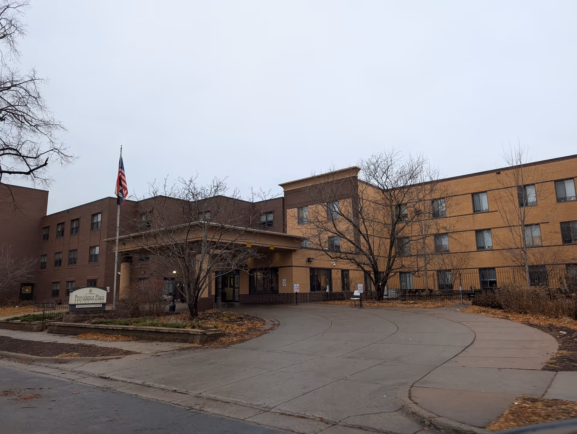 Front entrance of a multi-story brick building labeled "Providence Place" with a flagpole and circular driveway.