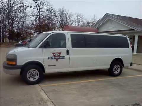 White shuttle van with Forsyth Care Center logo parked in a driveway near a building.