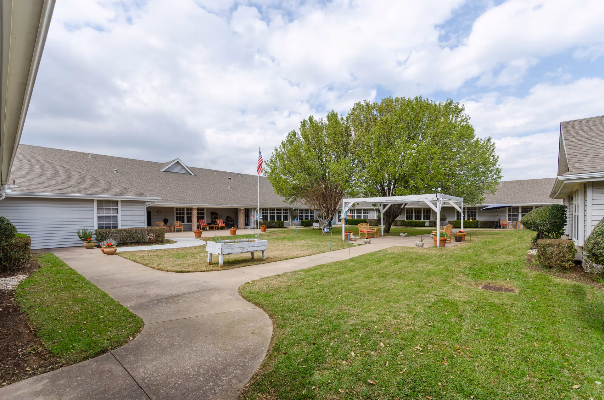 Courtyard of a senior living facility with a walkway, gazebo, trees, and lawn.