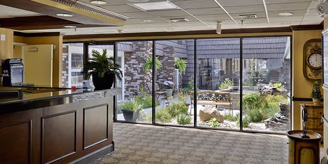 Reception area with a wooden desk and floor-to-ceiling windows looking out onto a landscaped courtyard with benches and plants.