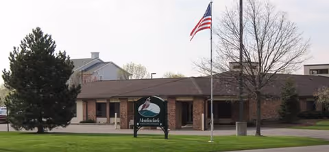 Exterior view of Meadowlark Retirement Village with flagpole and sign on green lawn.