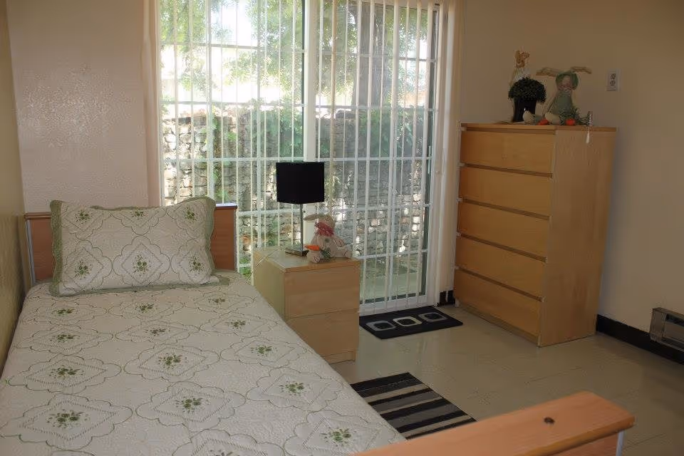 A tidy bedroom with a single bed, nightstand, dresser, and sliding glass door.