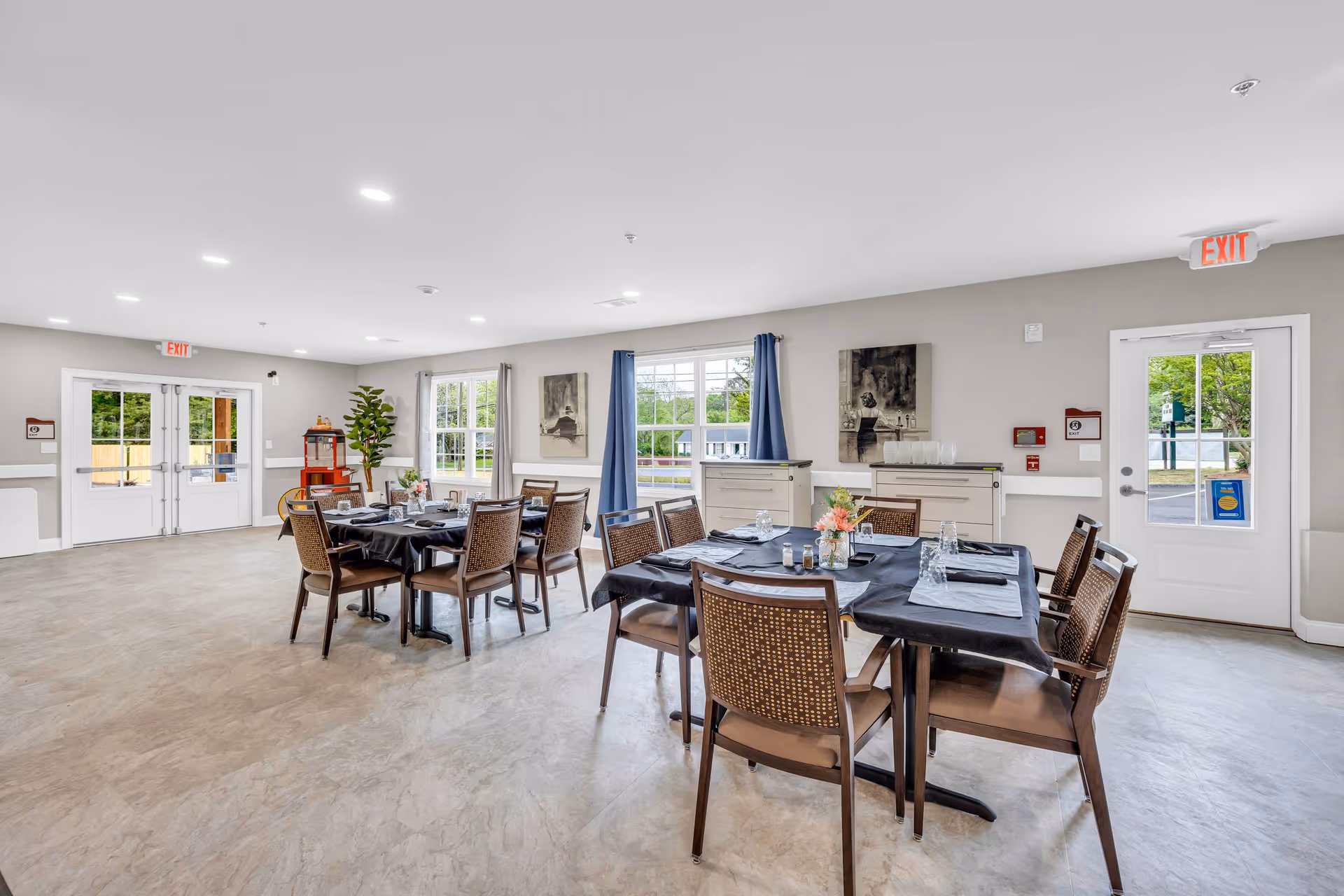 Bright communal dining room with tables set for meals and chairs in a senior living facility.