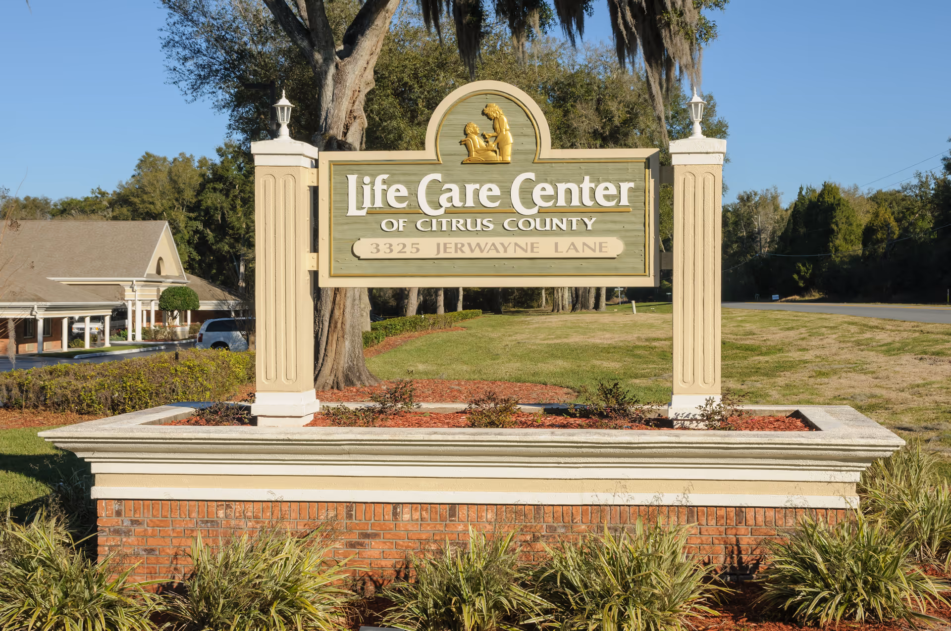 A large outdoor sign for Life Care Center of Citrus County located at 3325 Jerwayne Lane, set in a landscaped area with grass, bushes, and trees in the background under a clear blue sky.