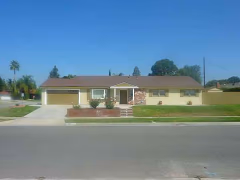 Single-story senior care facility with brick accents, driveway, front lawn, and entrance stairs.
