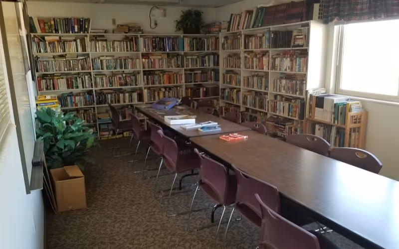 A long table with maroon chairs sits in a library-like room with book-filled shelves.