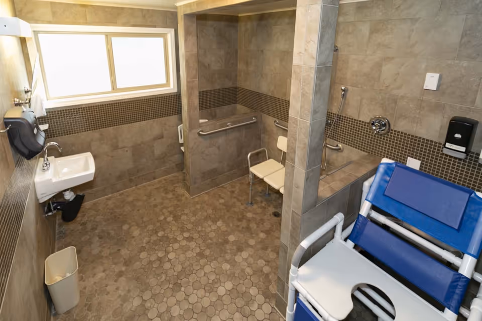 Accessible tiled bathroom with roll-in shower, grab bars, shower chair and transfer bench.