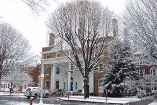 Front exterior of a brick, columned building with snow and leafless trees.