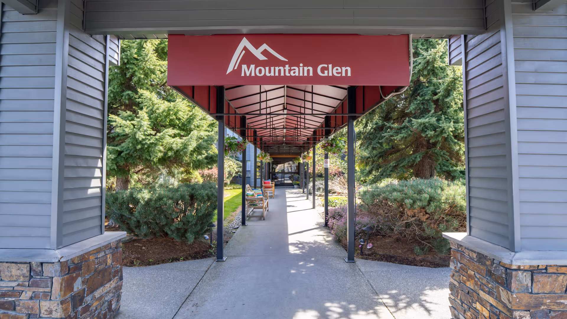 Covered entrance walkway with a red 'Mountain Glen' awning leading to the facility, flanked by shrubs and benches.