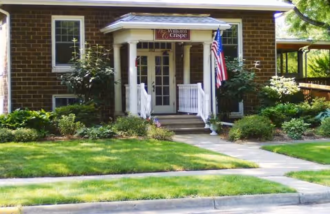Brick building entrance with white columns, stairs, and a William Crispe Community House sign.