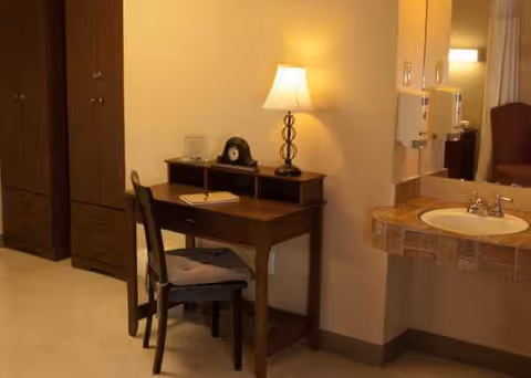 Desk, chair, and lamp beside a hall bathroom sink in a residential interior.