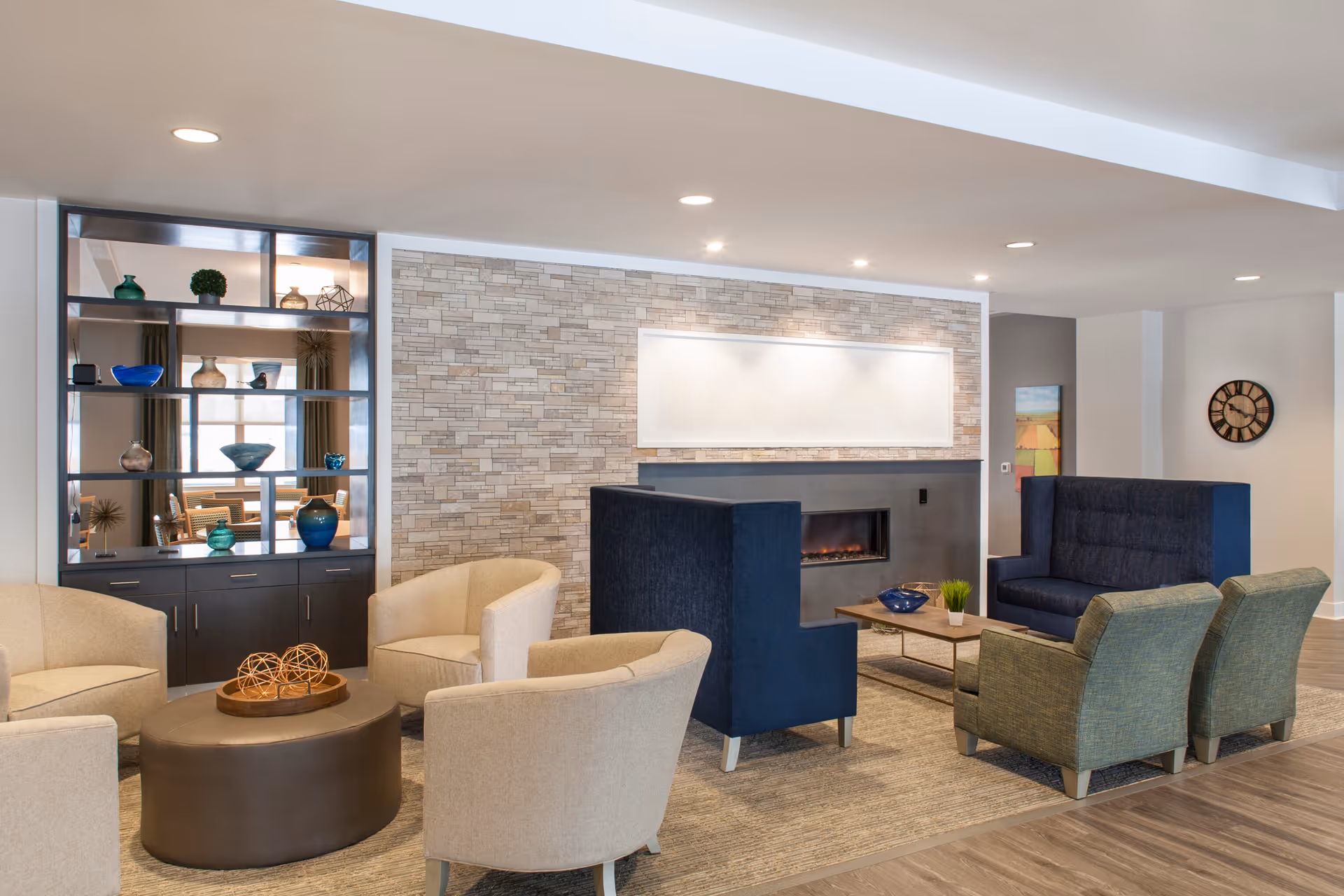 Modern lounge with multiple armchairs and sofas arranged around a fireplace and decorative shelving.