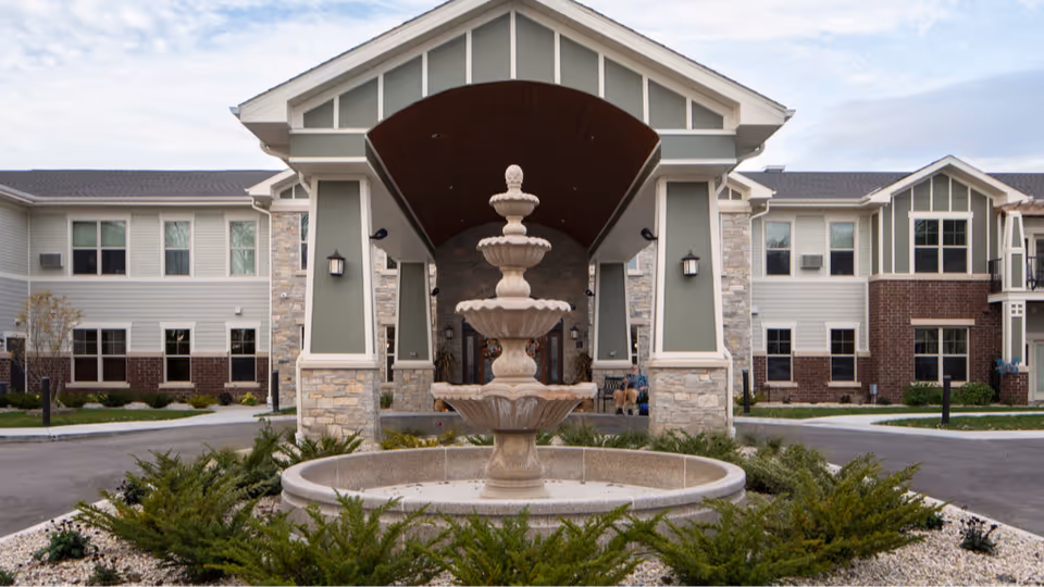 The covered main entrance of Heritage Senior Campus with a multi-tiered stone fountain in the foreground and a two-story building behind it.