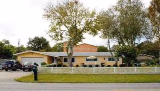 Front view of a single-story senior living facility with trees and a white fence.