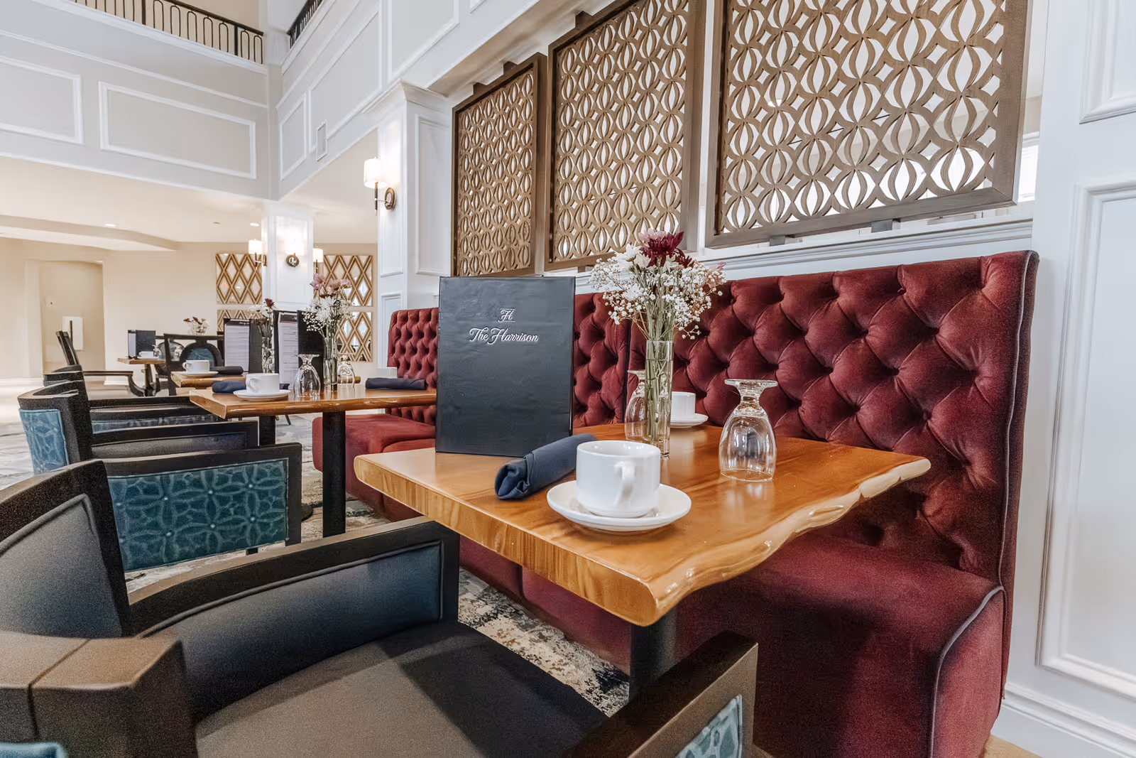 A dining area with tufted burgundy banquette seating, wooden tables set with cups and glassware, and decorative room dividers.