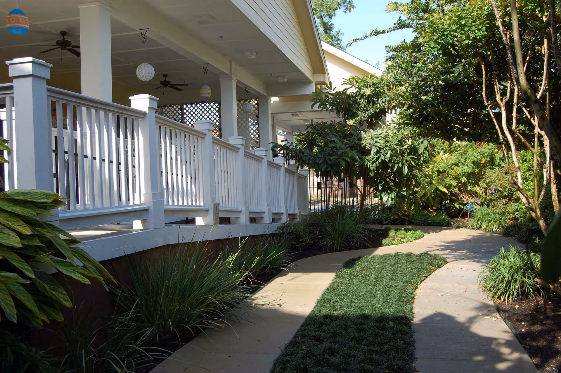 Outdoor walkway along a covered porch with white railings and lush landscaping.