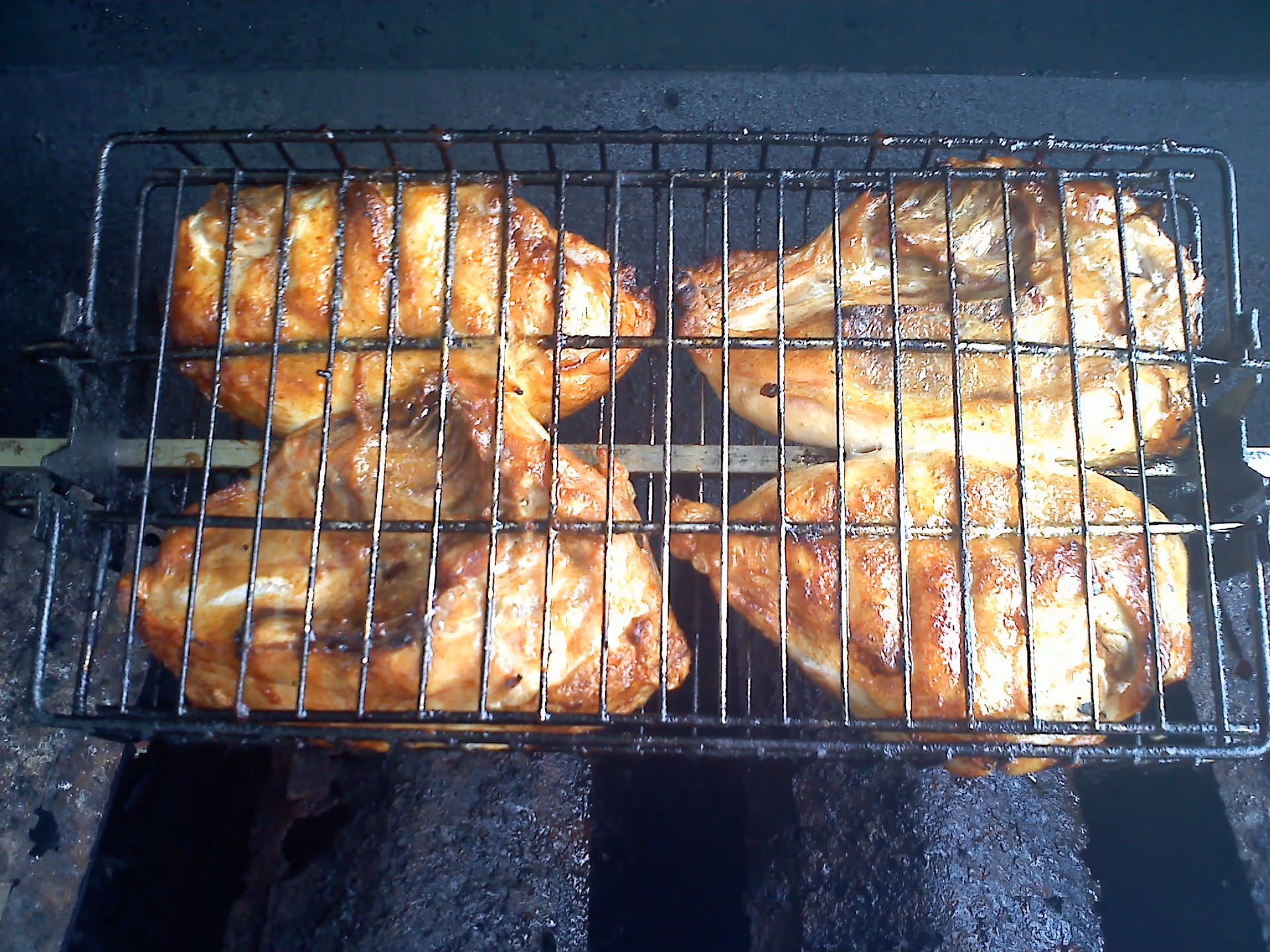Four pieces of grilled chicken cooking on a metal grill rack over a charcoal grill.