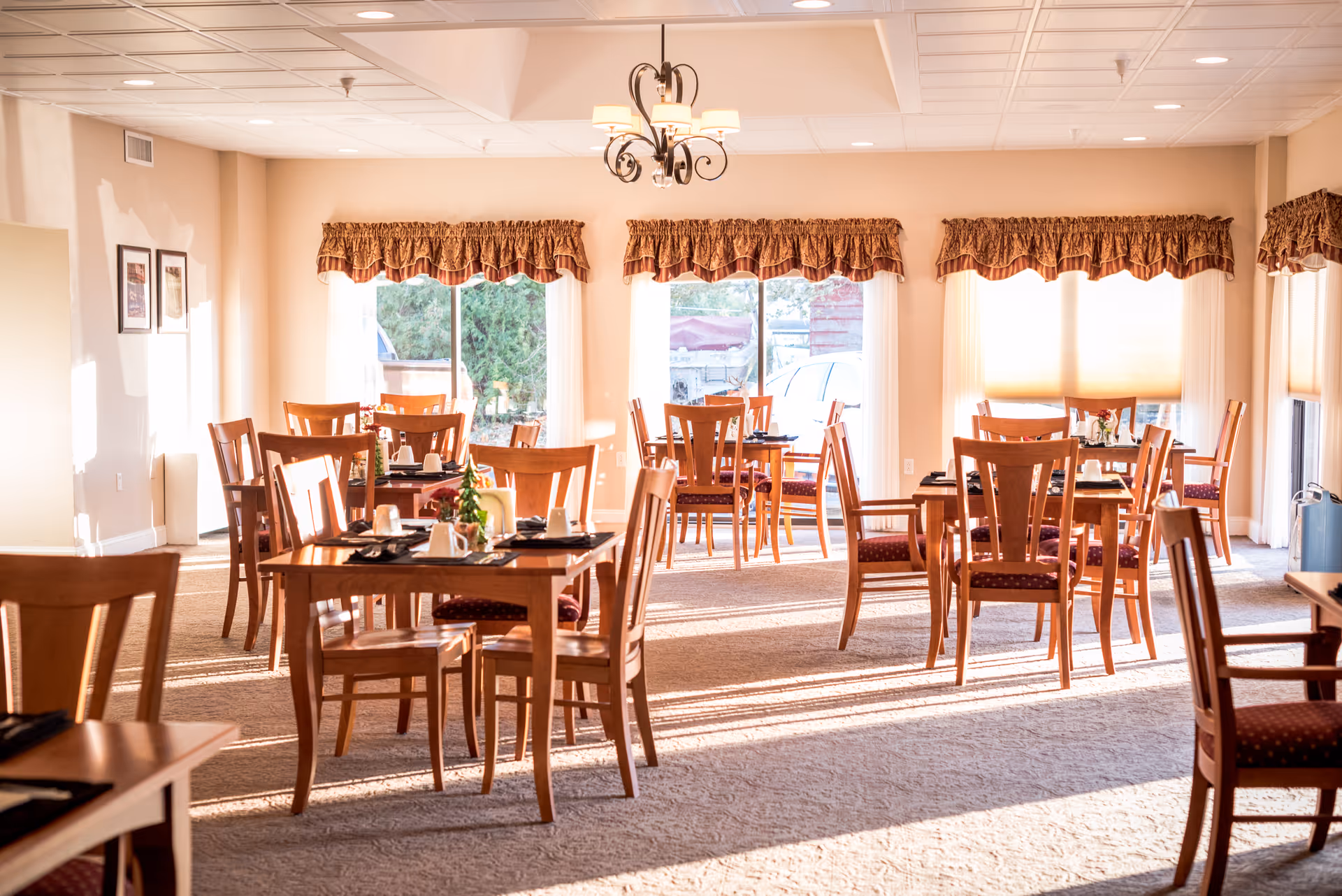 Sunlit dining room with multiple wooden tables and chairs arranged for meals.